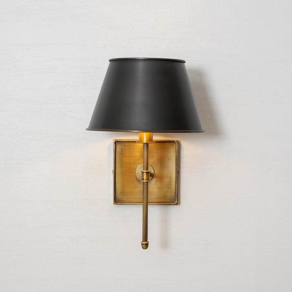 Rhodes wall sconce switched on, casting a warm glow down over the brass backplate with no glare